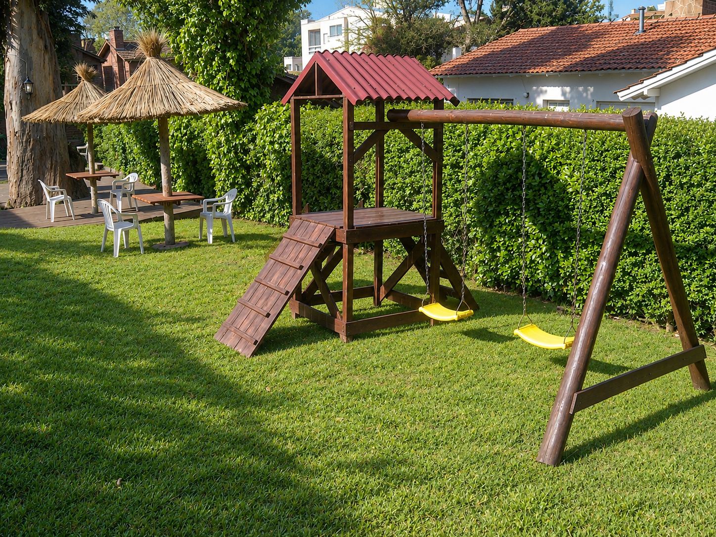 Juegos infantiles de madera con hamacas y tobogán sobre el pasto, junto a un cerco verde